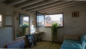 Une pièce dotée d’un plancher en bois, d’un lit, d’un lavabo et de deux fenêtres donnant sur un dôme et des bâtiments.