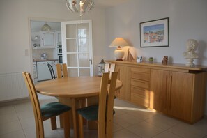 A dining area with a wooden table and chairs, a kitchen in the background, and a lamp on the counter.