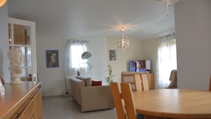 A modern living room with a dining area, a sofa, a television, and a chandelier. - YOUR HOLIDAY AT  SABLES D'OLONNE THE MOST BEAUTIFUL BEACH ON THE COTE DE LUMIERE (Le Château-d'Olonne)