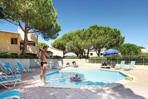 A swimming pool with lounge chairs and umbrellas, surrounded by trees and buildings.