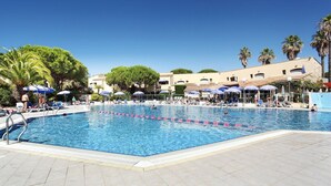 Una piscina con acqua cristallina, circondata da lettini e ombrelloni, con palme e edifici sullo sfondo.