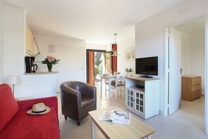 A living room with a sofa, a coffee table with a magazine, a television on a stand, and a dining area with a table and chairs.
