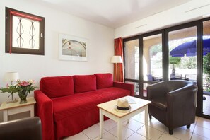 Ein rotes Sofa, ein kleiner Tisch mit einem Hut, ein Stuhl, eine Lampe und ein Fenster mit Vorhängen.
