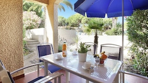 Una terrazza esterna con un tavolo apparecchiato per due persone, un ombrellone blu e diverse piante.