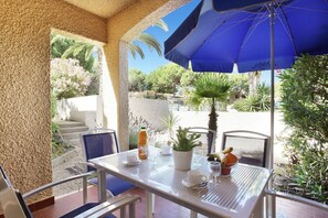 Eine Terrasse im Freien mit einem Tisch für zwei Personen, einem blauen Sonnenschirm und verschiedenen Pflanzen.