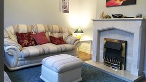 A living room with a sofa, ottoman, fireplace, and a painting on the wall. - House located in a private maintained estate. (Tralee)