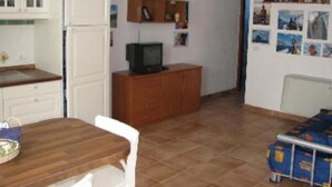 A compact kitchen with white cabinets, a wooden countertop, and a small television on a wooden cabinet.