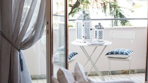 A balcony with a white table and two chairs, a white railing, and a view of trees and buildings.