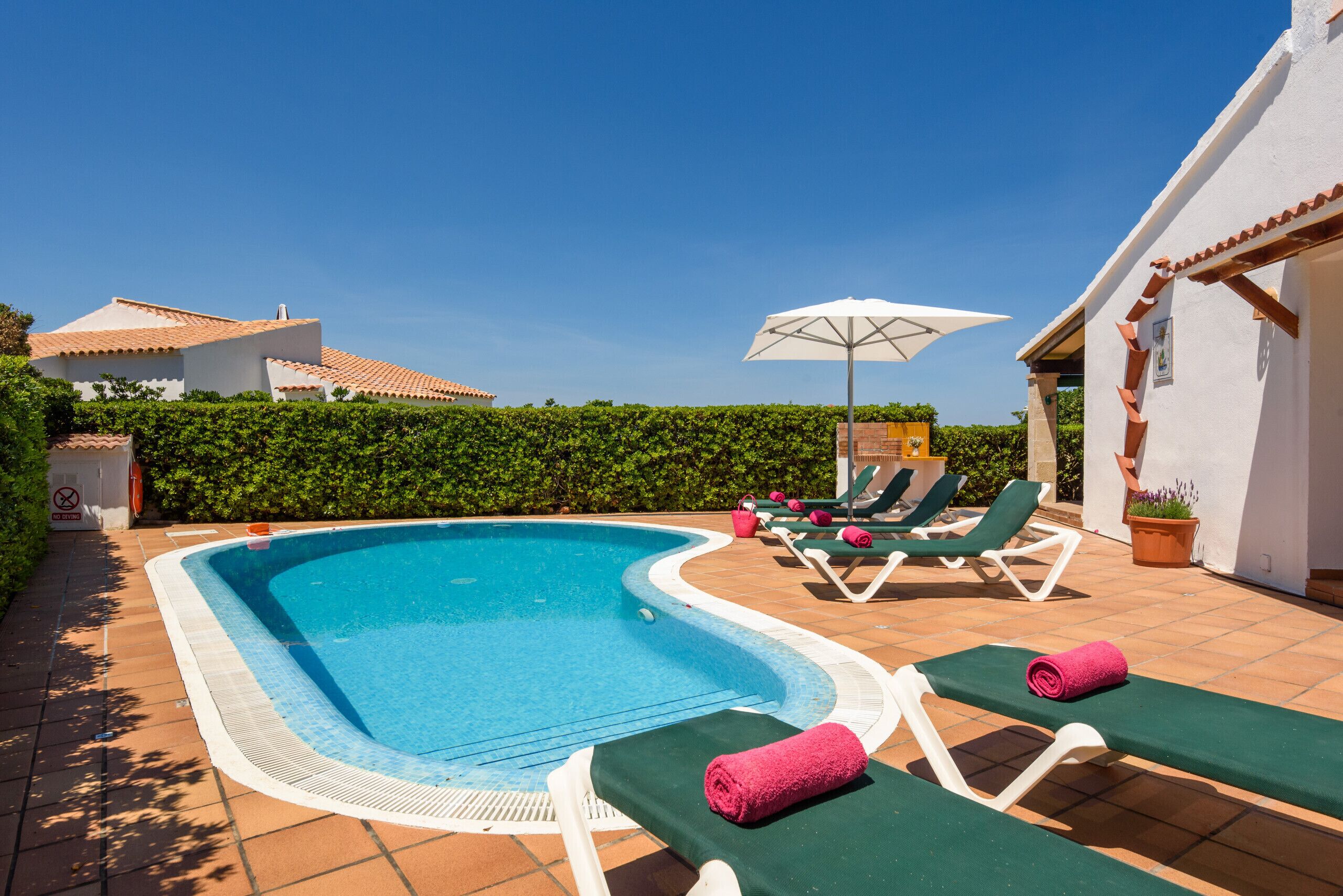 A swimming pool with lounge chairs and a sun umbrella.