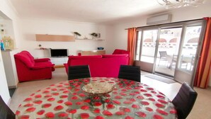 Una sala de estar con un sofá rojo, un televisor y una mesa de comedor con estampado de fresas.