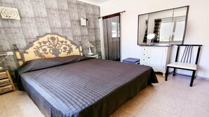 Un dormitorio con una cama grande, una mesita de noche con lámpara, un armario, una silla y un espejo.