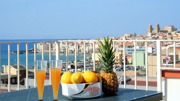 Ein Tisch mit einer Obstschale und zwei Gläsern Orangensaft, mit Blick auf eine Küstenstadt.