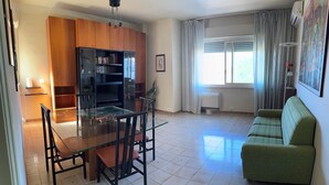 Ein Wohnzimmer mit einem Glastisch, Holzschränken, einem grünen Sofa und einem großen Fenster mit Vorhängen.