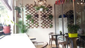 Un comedor con una pared de celosía de madera decorada con plantas en macetas, una araña y una mesa con sillas.