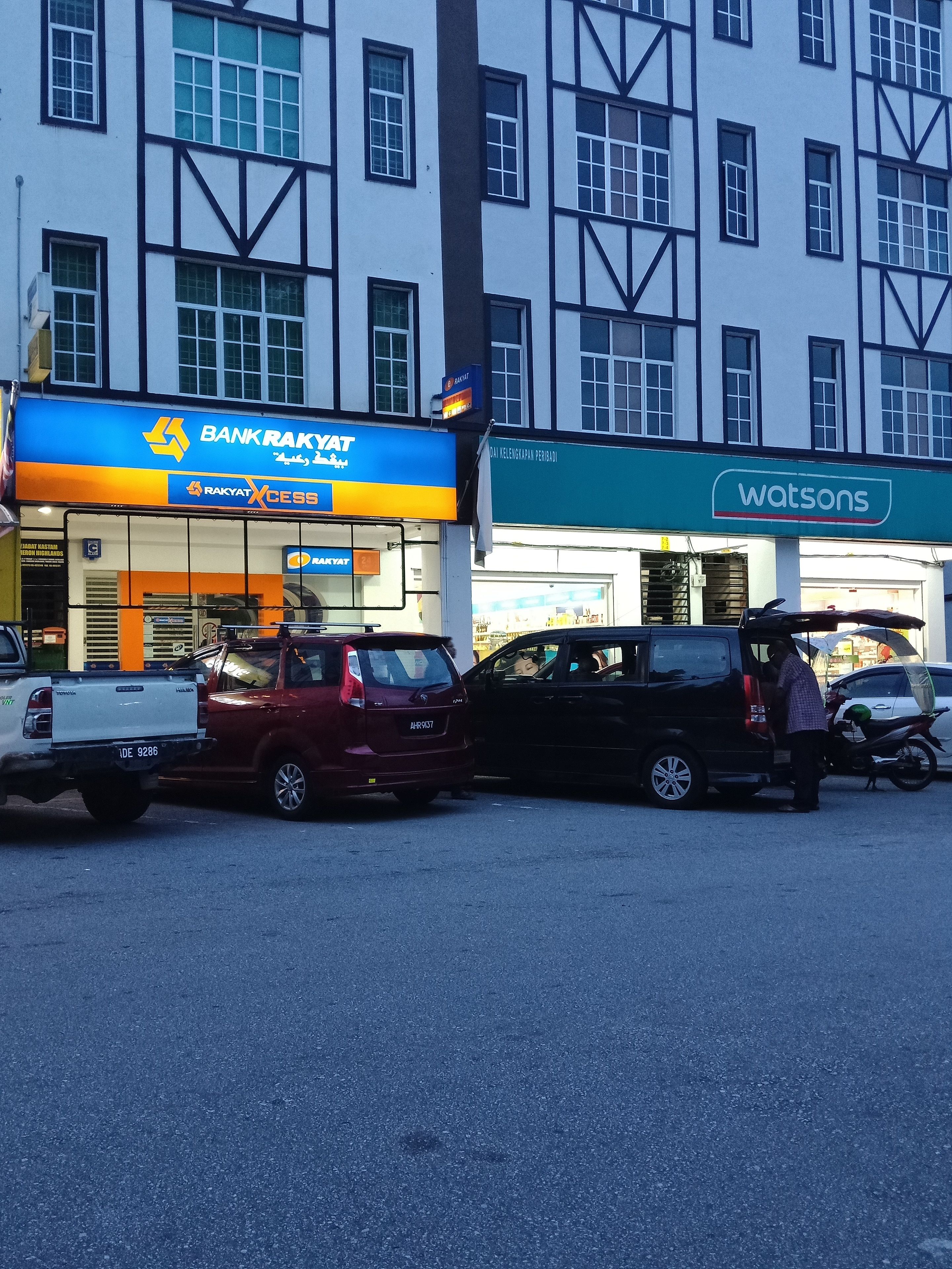A building with a blue and yellow sign for Bank Rakyat and a green sign for Watsons.
