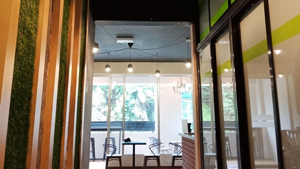 Un interior moderno con suelo de madera, detalles verticales verdes y vistas a un área de estar exterior.