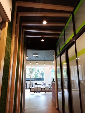 A modern interior with a wooden floor, green vertical accents, and a view of an outdoor seating area.
