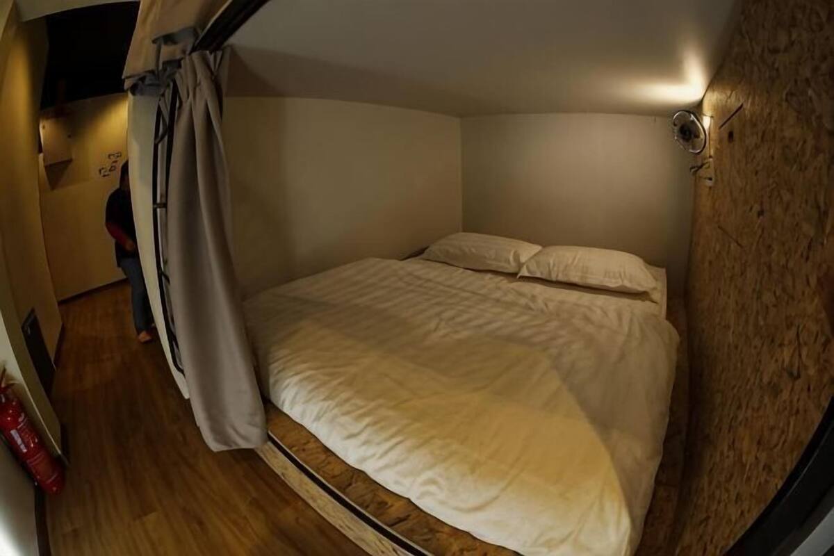 A small, cozy room with a bed, a curtain, and a wall-mounted light fixture.