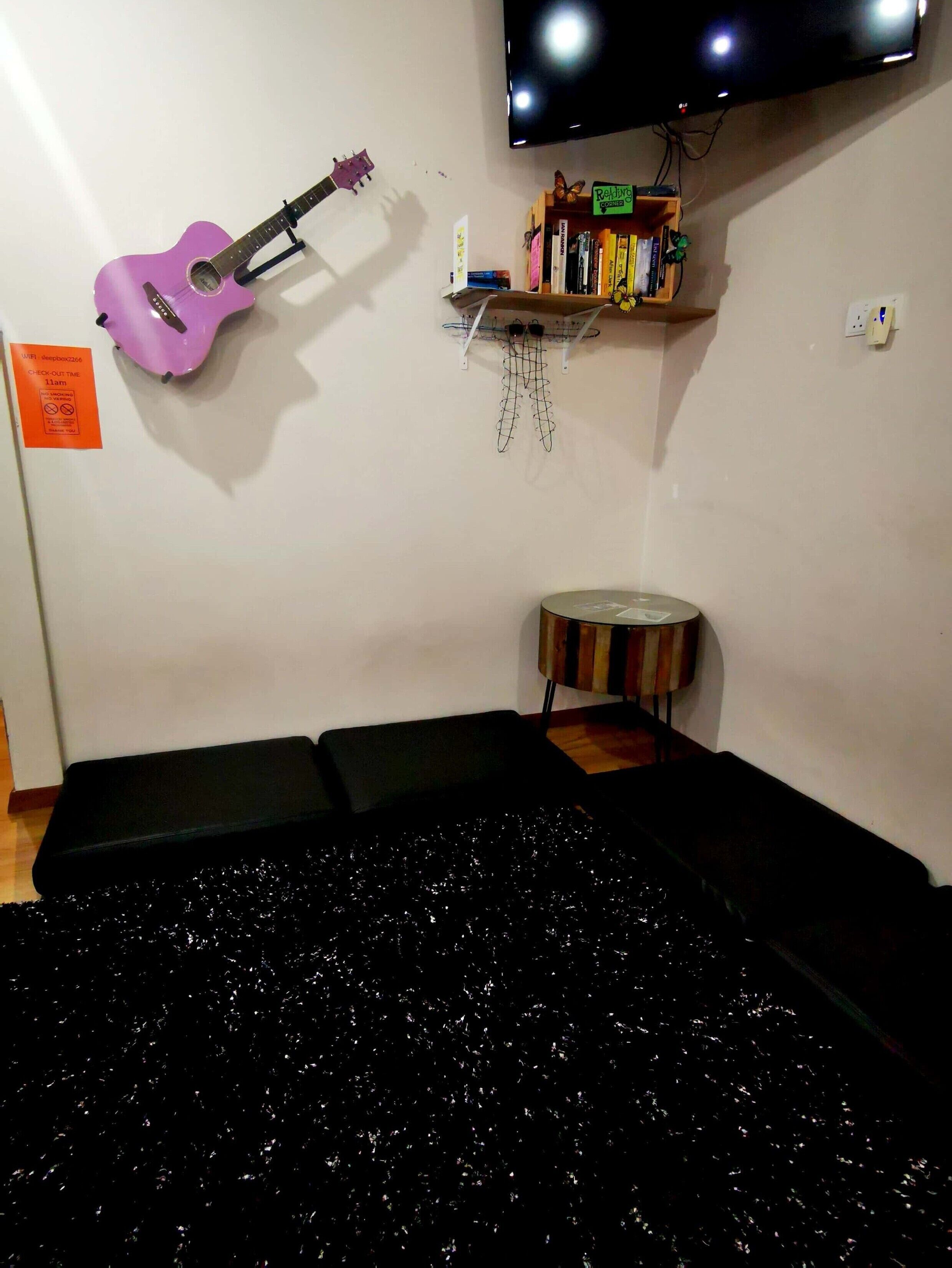 A room with a black couch, a purple guitar, a small round table, and a shelf with books and decorative items.