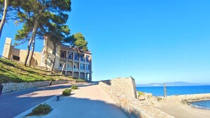 Ein Gebäude an der Küste mit einer Steinfassade, einem gepflasterten Weg und Blick aufs Meer.