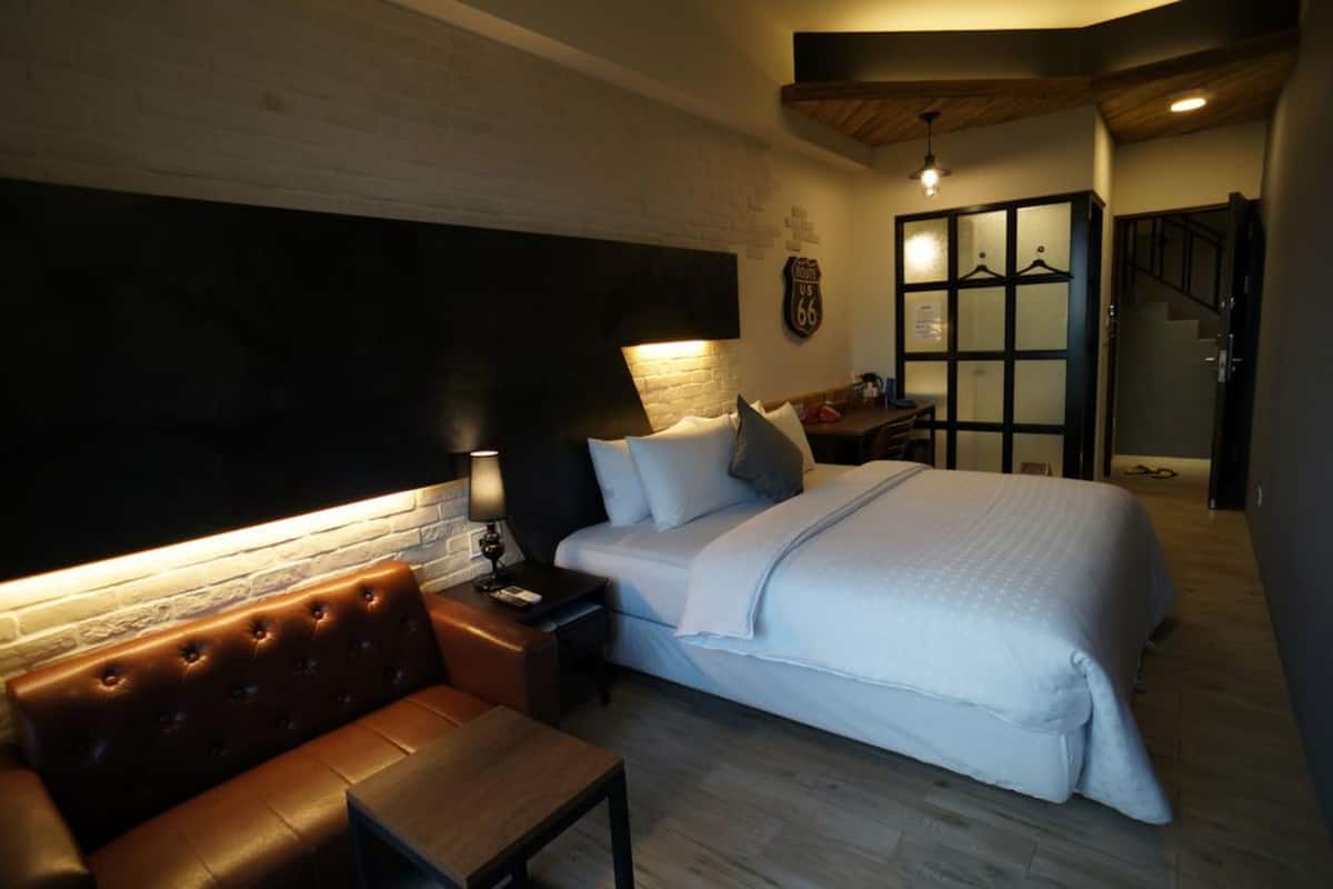 A bedroom with a large bed, a nightstand, a leather bench, a wall-mounted TV, and a staircase.