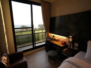 A hotel room with a large window, a desk with a lamp, a bed, and a leather chair. - Kenting Moon Bay Hotel (Hengchun)