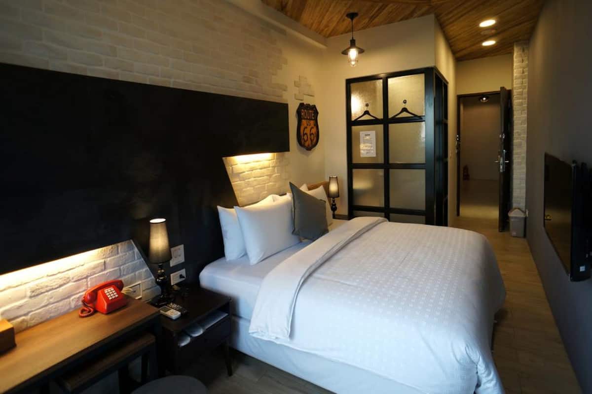 A hotel room with a large bed, a desk with a telephone, a wardrobe with a mirror, and a wall-mounted TV.