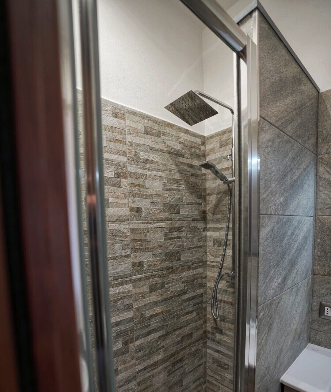 Eine Dusche mit Glastür, Wänden aus Steinplatten und einer Duschbrause.