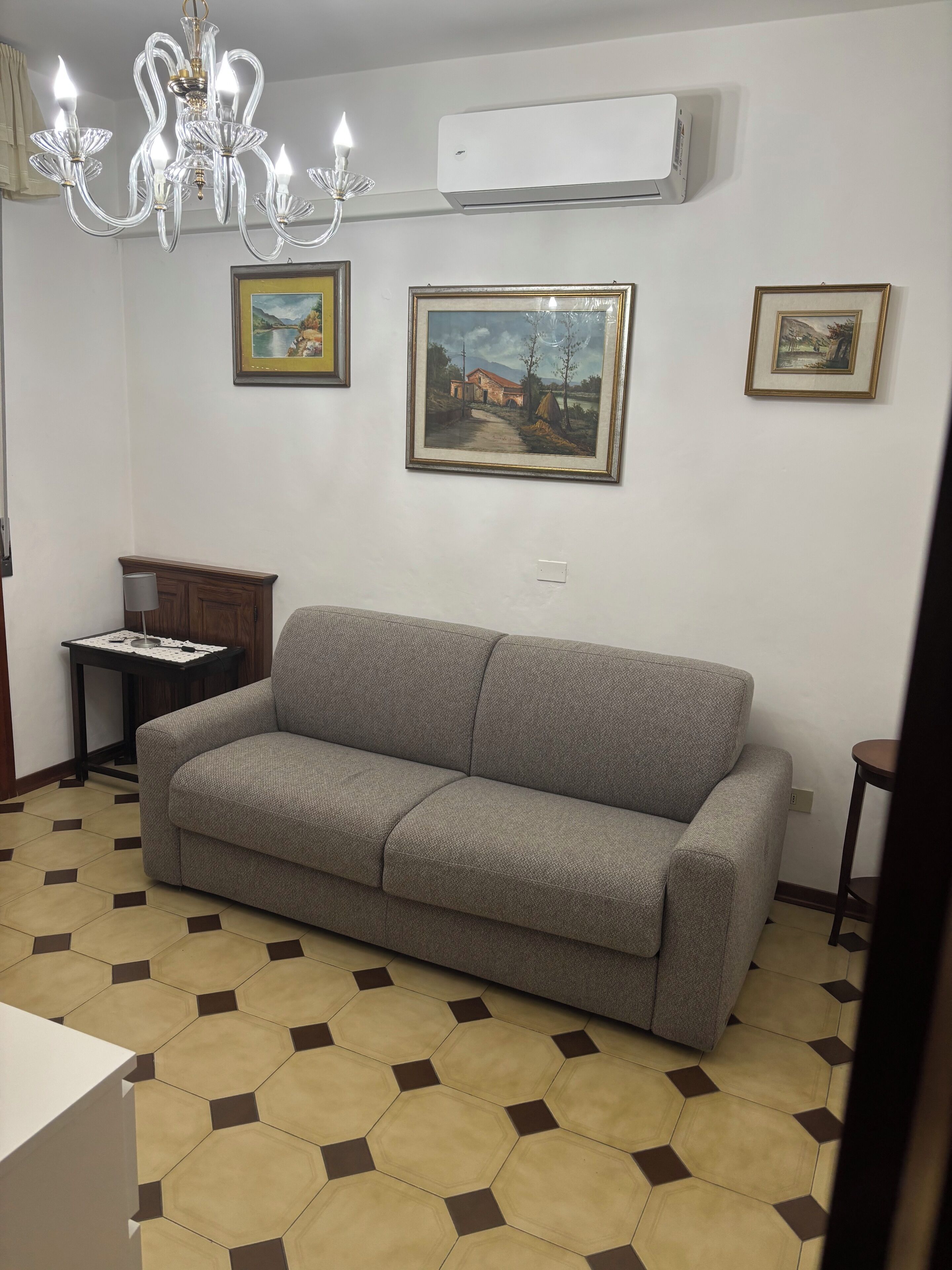 Un salon avec un canapé gris, un lustre et trois tableaux encadrés accrochés au mur.