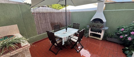 Um pátio com mesa, cadeiras, churrasqueira e um vaso de planta.