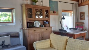 En hyggelig stue med en sofa, et træskab med glaslåger, et spisebord med stole og et vindue med gardiner.