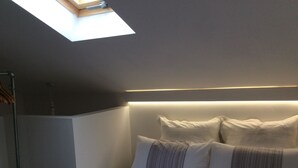Een slaapkamer met dakraam, een bed met wit en gestreept beddengoed en een bedlamp.