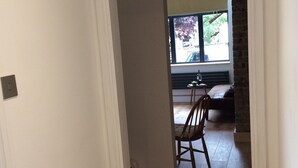 Een gang die uitkomt in een eetruimte, met een houten vloer, een stoel en een tafel waarop een fles en een glas staan.