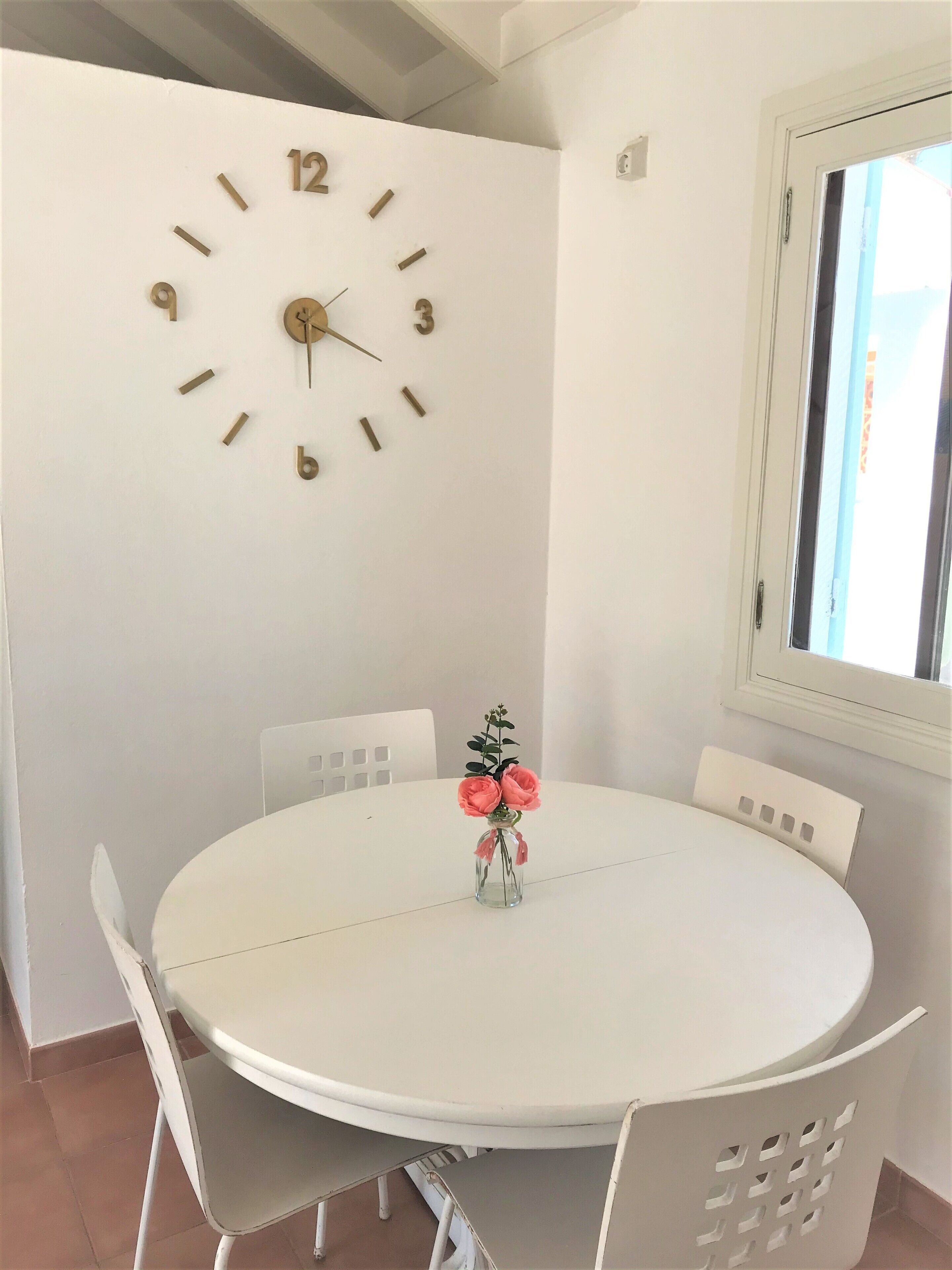 Ein runder Esstisch mit weißen Stühlen, einer Wanduhr und einer Blumenvase.