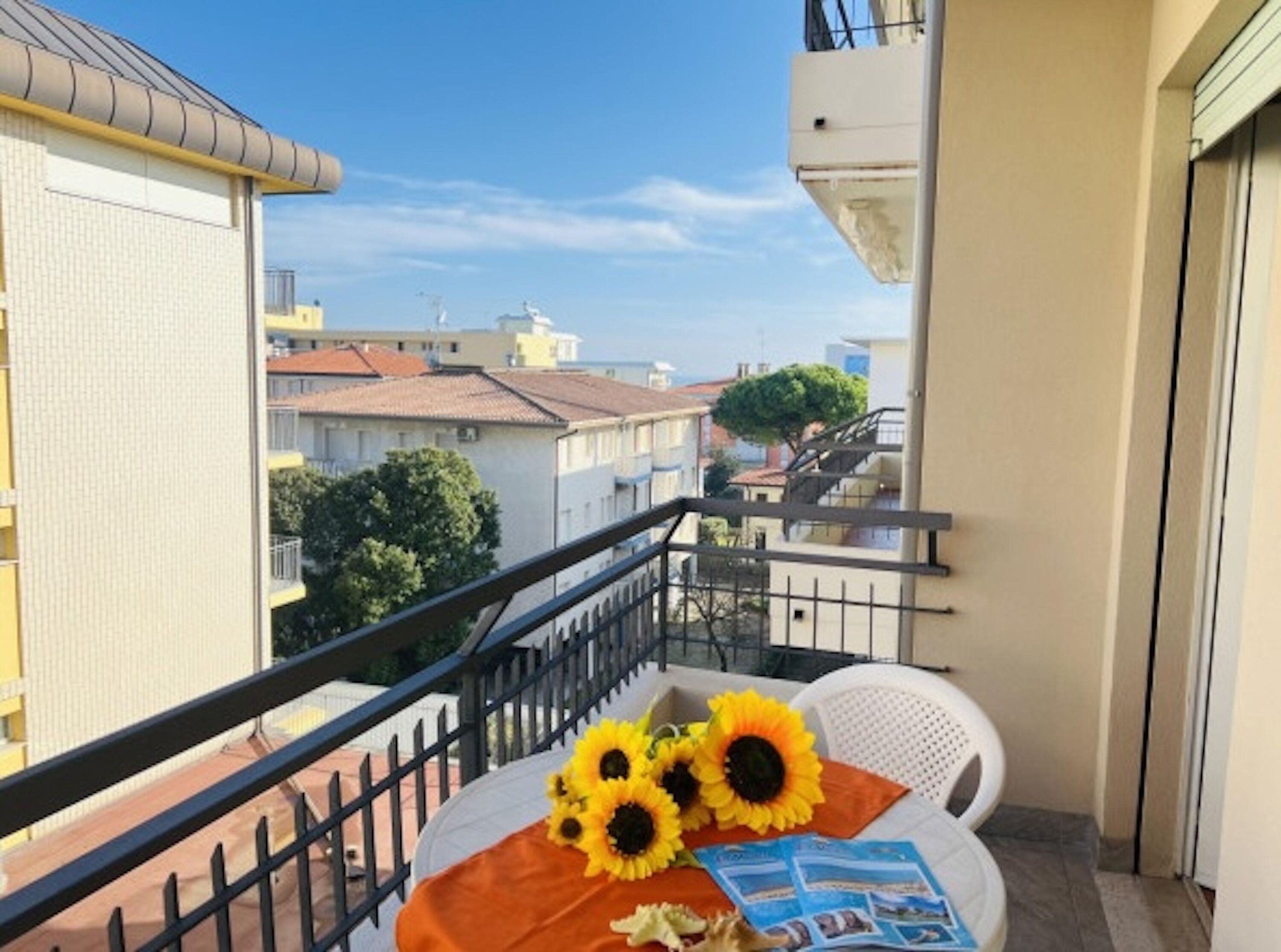 Un balcon avec une chaise blanche, une table ornée de tournesols et une vue sur des immeubles.
