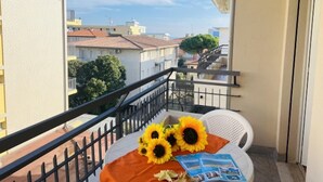 Ein Balkon mit einem weißen Stuhl, einem Tisch mit Sonnenblumen und Blick auf Gebäude.
