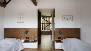 A room with two beds, wooden headboards, and a small table with a lamp and glass.