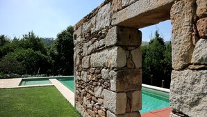 A stone archway leading to a swimming pool area with a well-maintained lawn and a clear view of the surrounding trees.