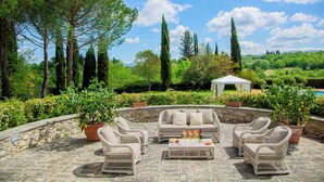 An outdoor seating area with wicker furniture and a stone floor, surrounded by greenery and a clear sky. - EXCLUSIVE CHIANTI VILLA SPECTACULAR POOL TENNIS COURT 15 MIN TOFLORENCE   (IMPRUNETA)