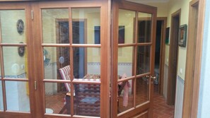Ein Zimmer mit Holztür, Fliesenboden, einem Tisch mit Blumenmuster-Tischdecke und einem Streifenstuhl.