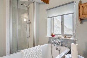 Een badkamer met een douchecabine, een bad met een handdoek, een raam met uitzicht en een plank met decoratieve spullen.