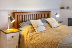 Een keurig opgemaakt bed met een houten hoofdbord, twee bedlampjes en een witte nachtkastje met lades.
