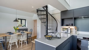 Una cocina moderna con una isla central, horno empotrado y microondas. Cuenta con un comedor con mesa y sillas de madera, y una pequeña isla de cocina con un cuenco de fruta.