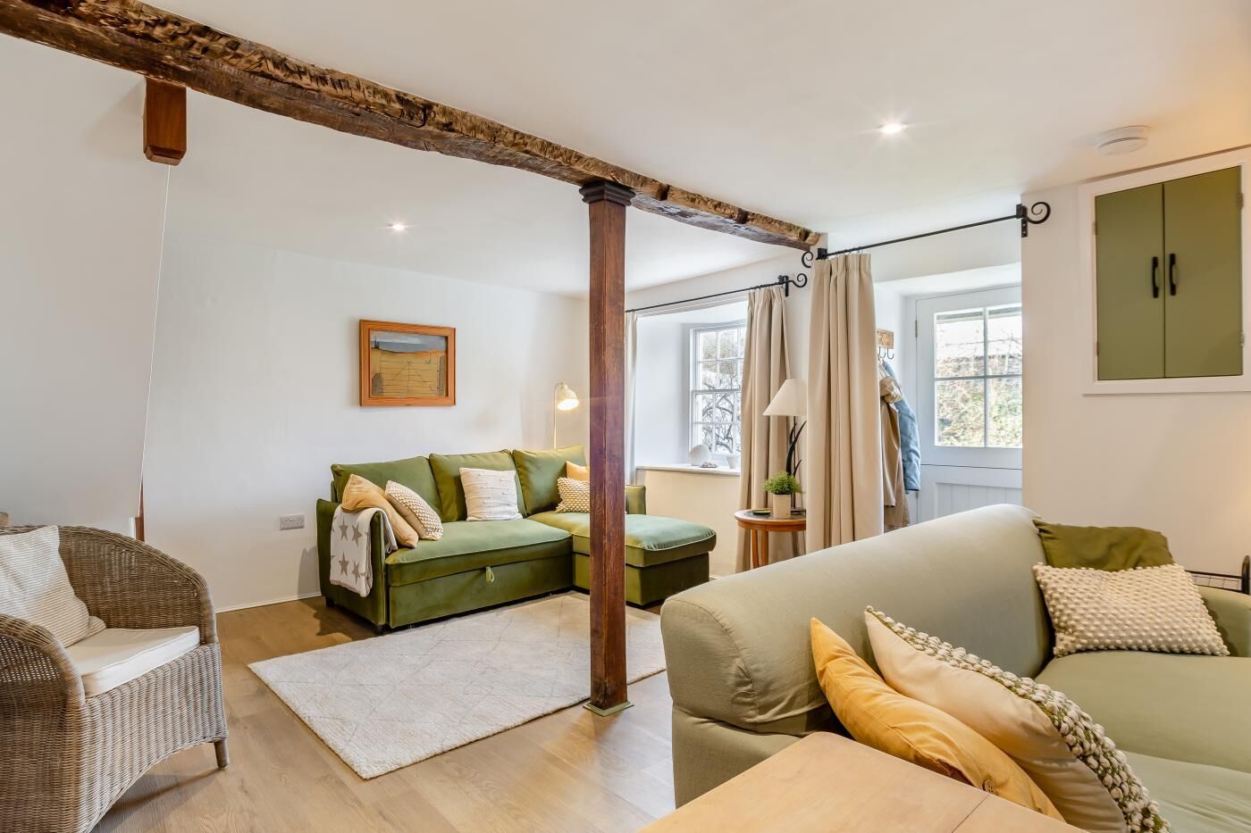 A cozy living room with a green sofa, a wicker chair, and a wooden beam ceiling.