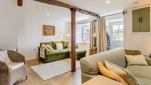 Una sala acogedora con un sofá verde, una silla de mimbre y techo con vigas de madera.