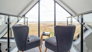 Una habitación moderna con un tragaluz triangular grande, dos sillones tapizados en gris y una mesita con una taza y un libro.