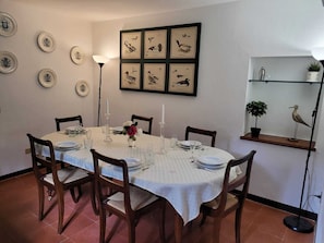 A dining room with a round table set for four, surrounded by wooden chairs. There are framed bird illustrations on the wall above the table.