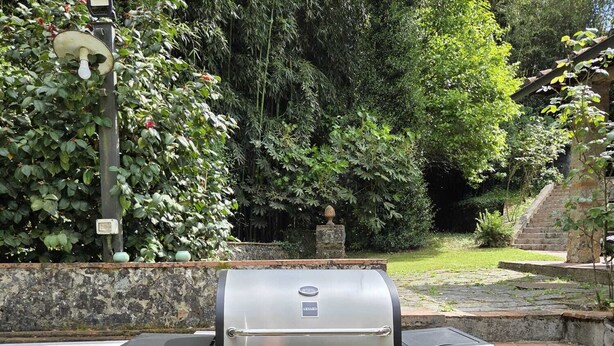 Een draagbare gasgrill met een digitaal display, een zijschuifkastje met twee lades, en een achtergrond van een stenen muur.
