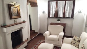 Een woonkamer met een open haard, een witte fauteuil, een bank en een kamerbreed tapijt.