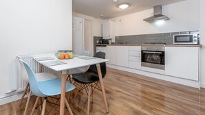 A modern kitchen with white cabinets, a microwave, an oven, and a dining area with a table and chairs. - Royal Apartments RA2 (Greater London)